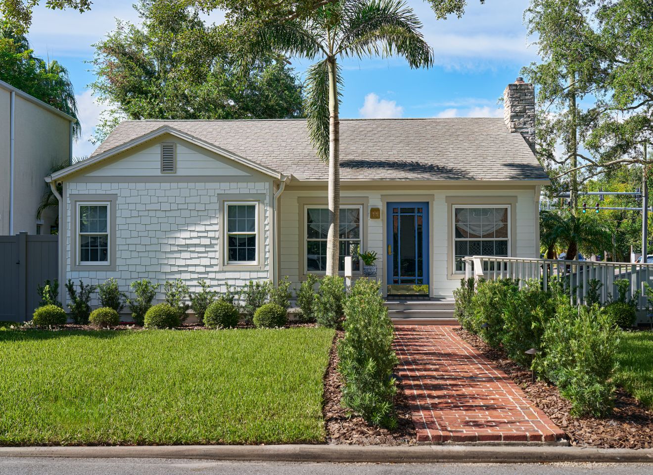 The Bayshore Rose bungalow, with a blue front door, white porch railing and a brick walk